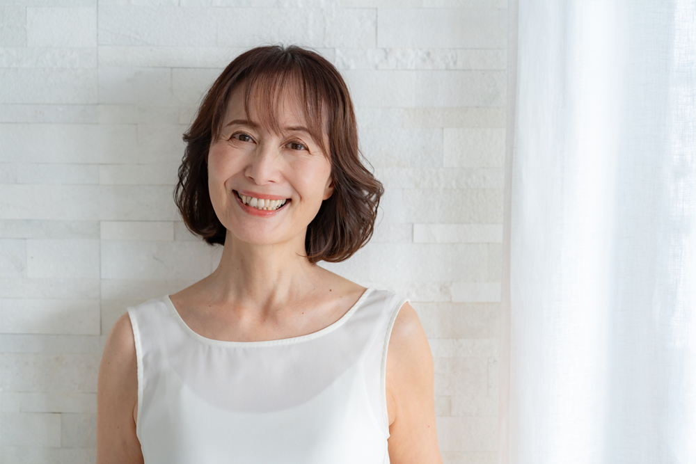 50代女性が河辺とカーテンが白い部屋で笑っている